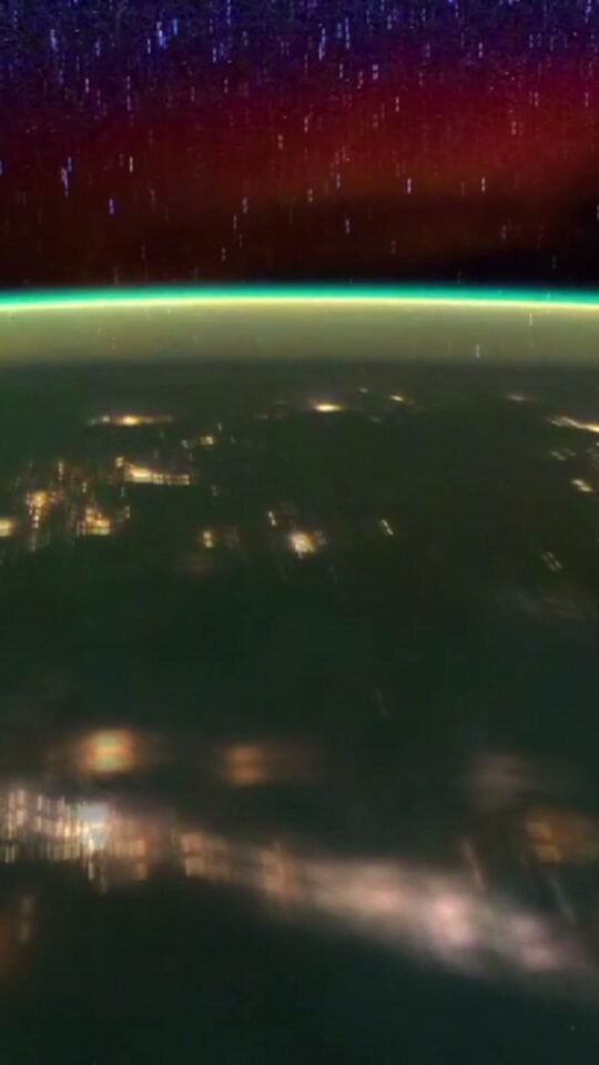 Earth’s city lights beneath green airglow and a red night sky
